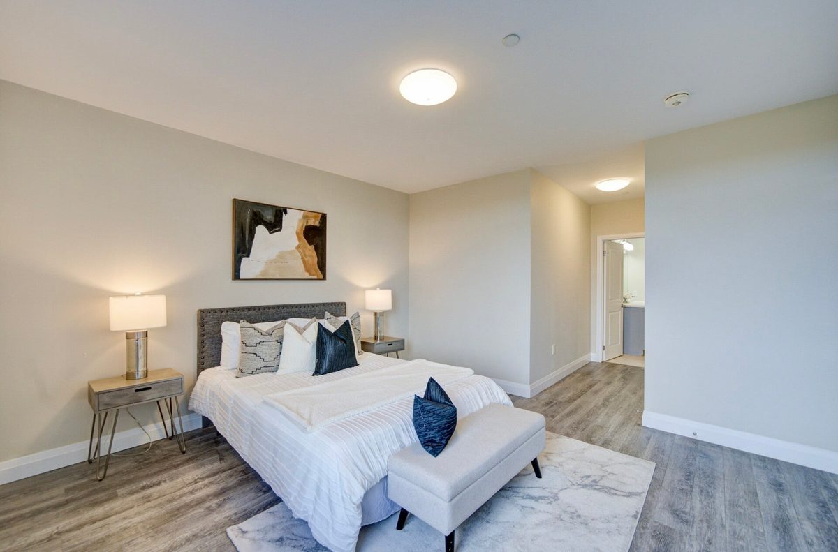 A cleaned bedroom with a made white bed, navy cushions and a bench at its foot
